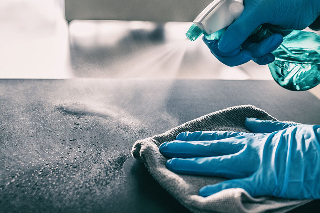 Manos con guantes desinfectando una superficie con spray